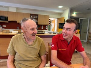 Senior lächelt mit Pfleger im Gemeinschaftsraum, begleiten sich im Alltag für bessere Lebensqualität.