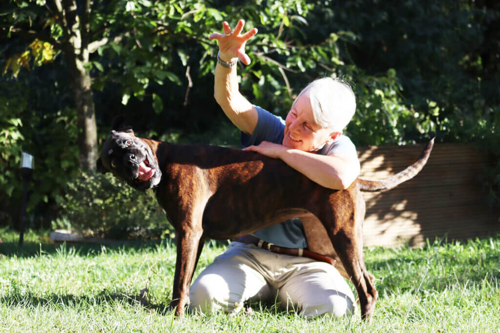 Ältere Person spielt freudig mit ihrem Hund im Garten bei sonnigem Wetter.