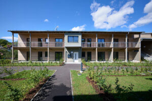 Modernes zweistöckiges Gebäude mit Holzfassade und Garten vor blauem Himmel.