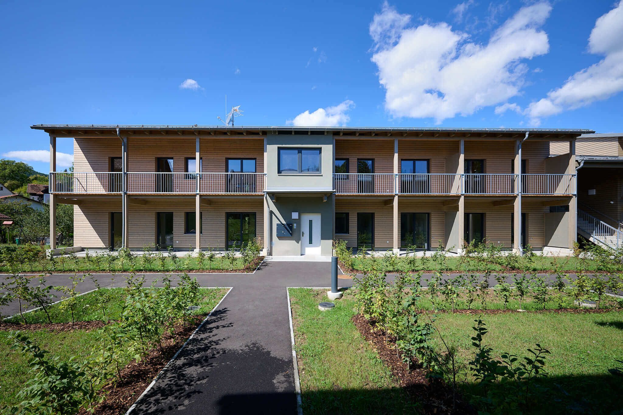 Modernes zweistöckiges Gebäude mit Holzfassade und Garten vor blauem Himmel.