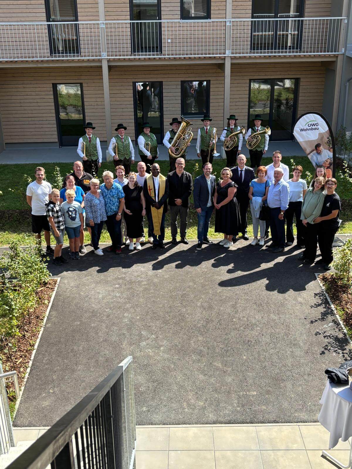 Gruppenfoto vor einem Gebäude mit traditioneller Blaskapelle, Bewohnern und einem Banner von OWG Wohnbau.