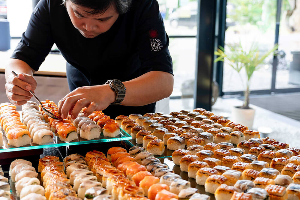 Koch dekoriert mit Präzision Sushi-Platten im Restaurant, frische Zutaten sorgfältig arrangiert. Japanische Küche genießen.