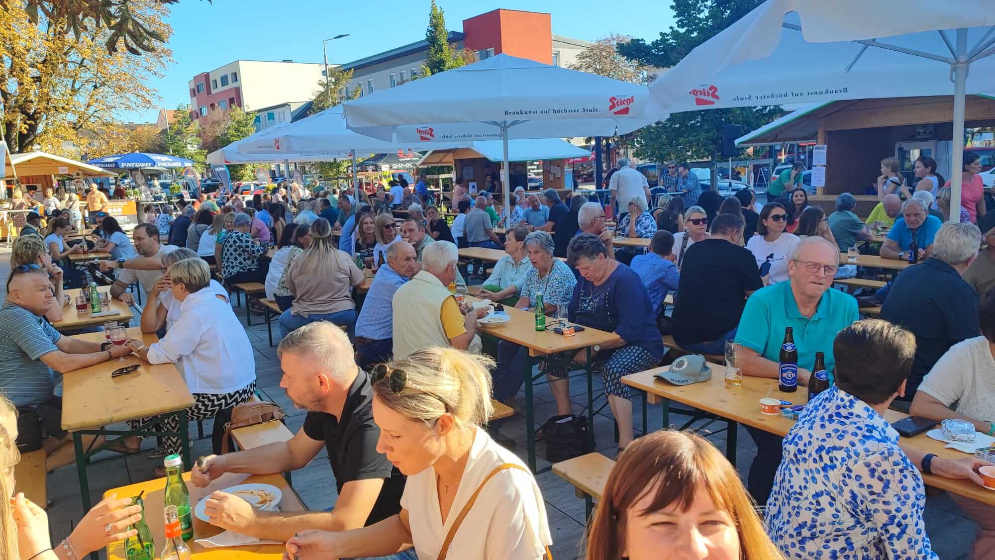 Menschen genießen ein geselliges Beisammensein in einem sonnigen Biergarten mit Tischen und Sonnenschirmen.