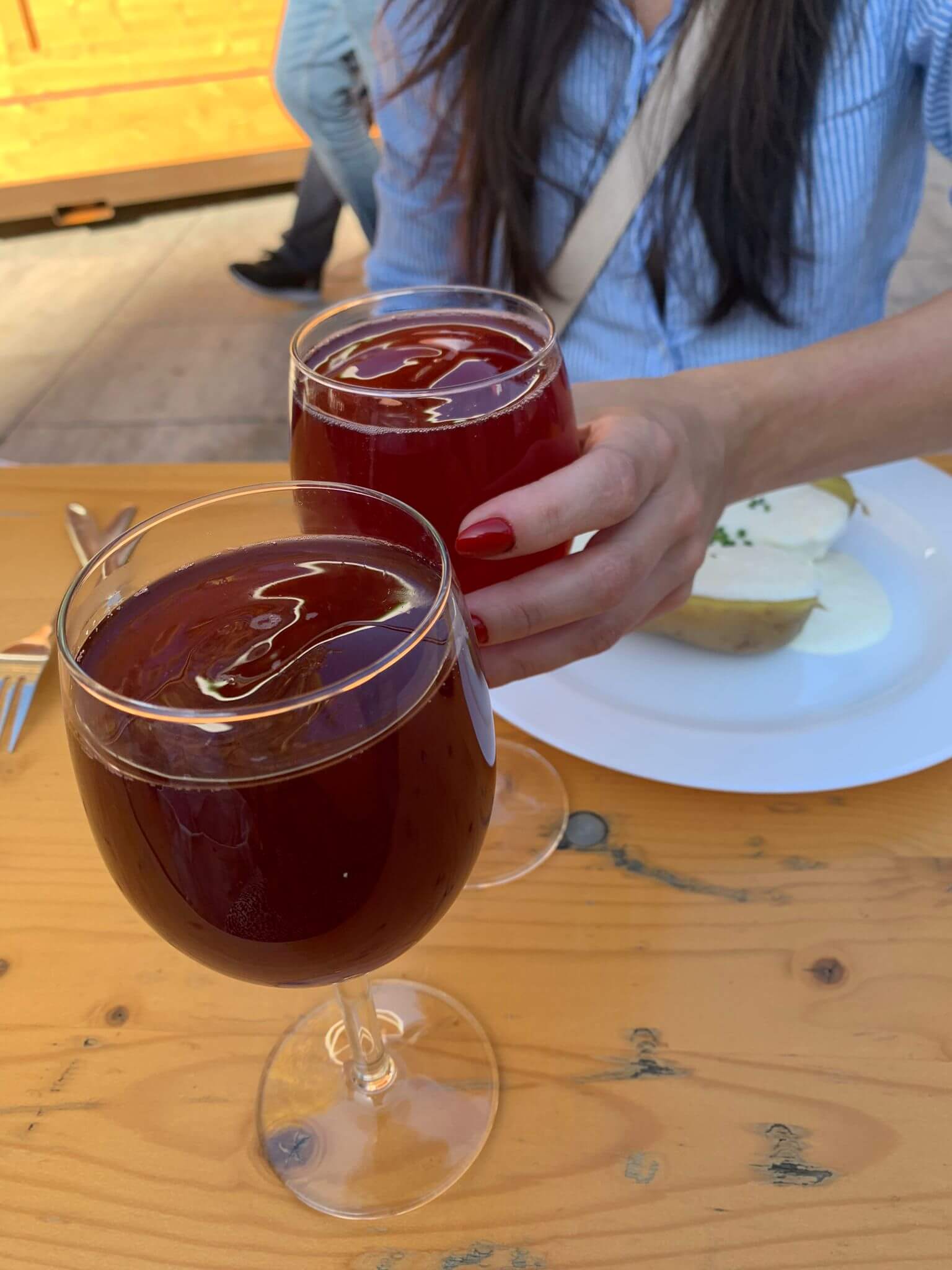 Zwei Gläser Rotwein beim Anstoßen auf einem Holztisch, begleitet von einem Teller mit Käse.