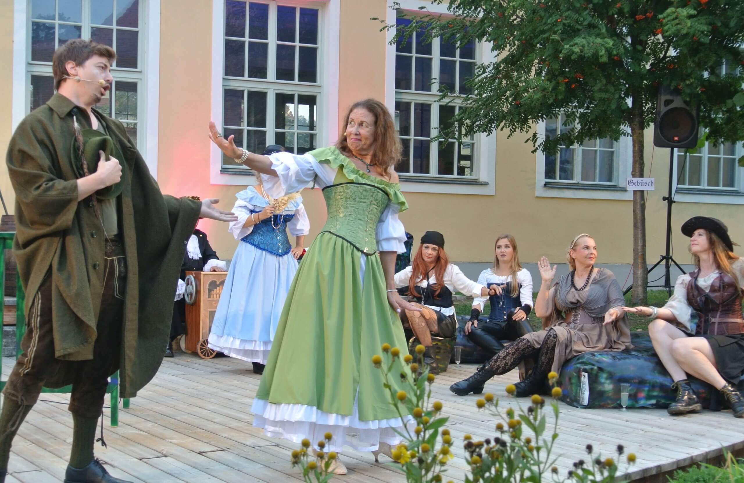 Schauspieler führen ein historisches Drama in aufwendigen Kostümen auf einer Freiluftbühne auf.