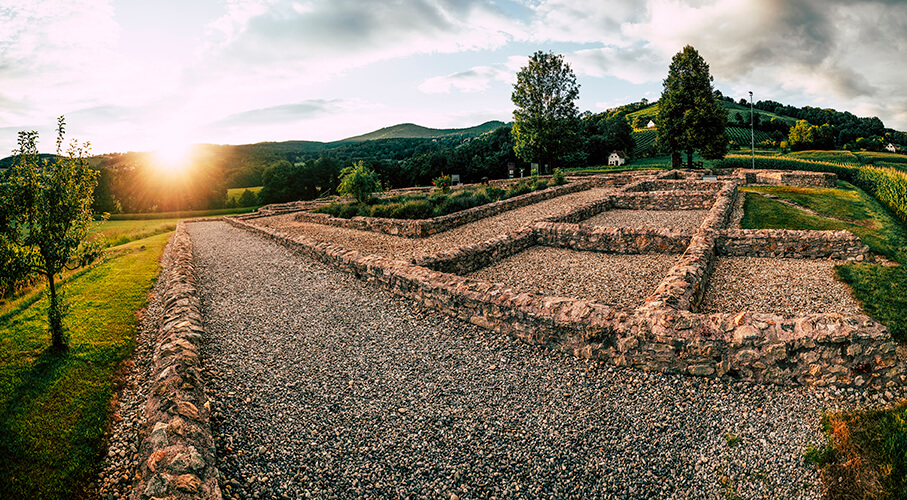 Römische Ruinen bei Sonnenuntergang im Grünen, umgeben von Bäumen und Hügeln – malerische Landschaft.