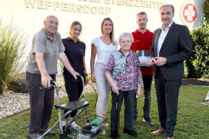 Senioren und Pflegekräfte posieren vor dem Kompetenzzentrum Weppersdorf, im Freien bei Sonnenschein.