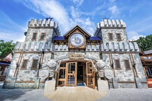 Mittelalterliches Restaurant mit Burgfassade und Ritterskulpturen unter blauem Himmel im Freizeitpark.