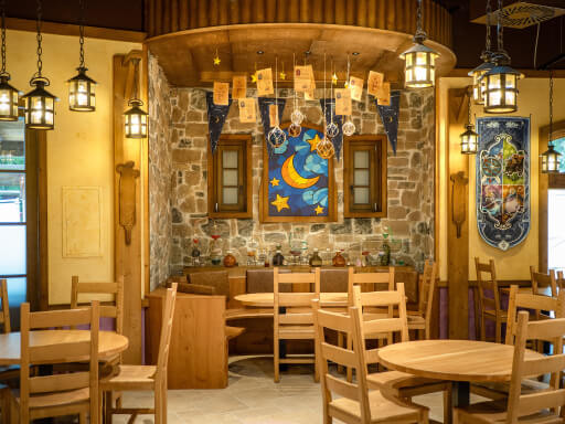 Gemütliches Café mit Holzmöbeln und Wanddekoration im Fantasie-Stil, beleuchtet von hängenden Laternen.