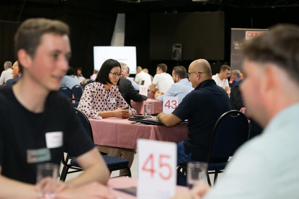 Geschäftsleute bei einer Networking-Veranstaltung, diskutieren an Tischen mit Nummern in einem Konferenzraum.