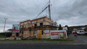 Baustelle eines Wohnungsbauprojekts in einer kleinen Stadt, Bauarbeiter arbeiten unter bewölktem Himmel, Kran im Hintergrund.