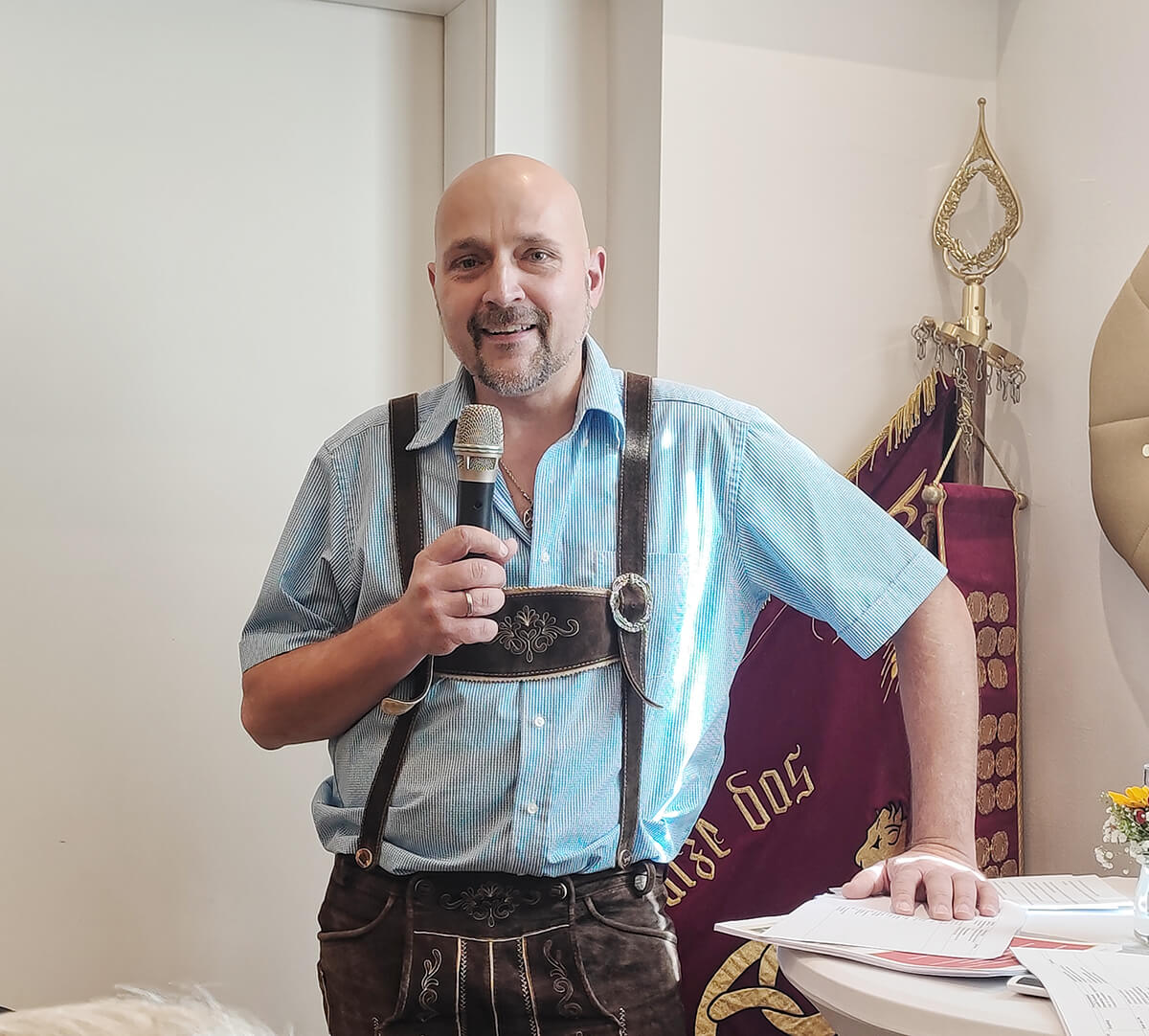 Ein Mann in traditioneller Tracht spricht mit Mikrofon bei einem regionalen Event, symbolisch für kulturellen Qualitätsjournalismus.