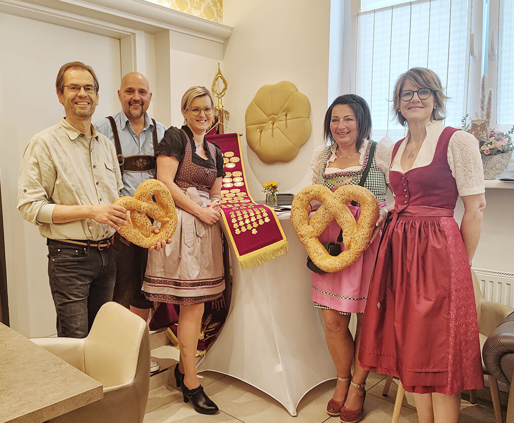 Eine Gruppe in traditioneller Tracht präsentiert große Brezeln und Auszeichnungen, ideal für regionales Magazin wie Prima Magazin.