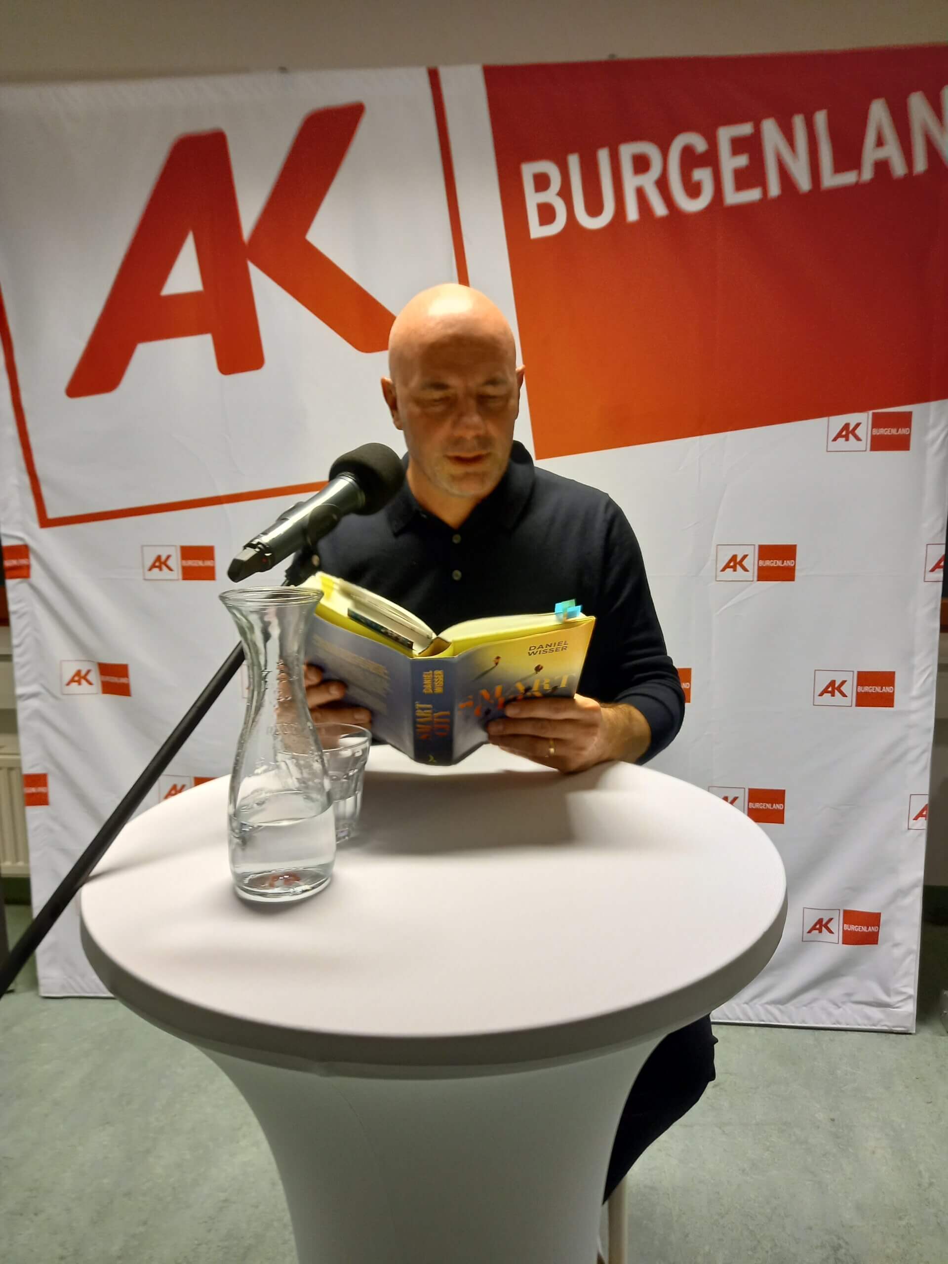 Ein Mann liest vor Publikum aus einem Buch bei einer Veranstaltung der Arbeiterkammer Burgenland.