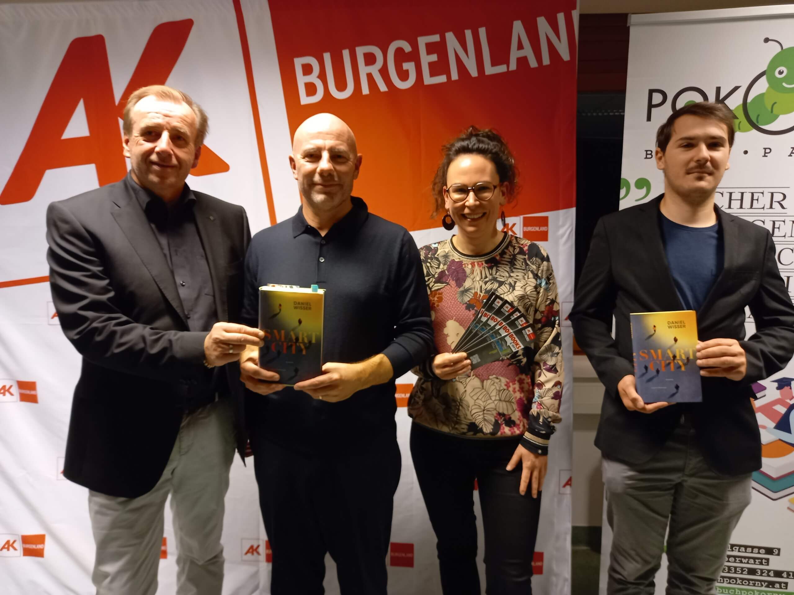 Gruppe von vier Personen präsentiert beim Buch-Event Smart City im Burgenland ihre Exemplare, lächelnd vor Bannern.