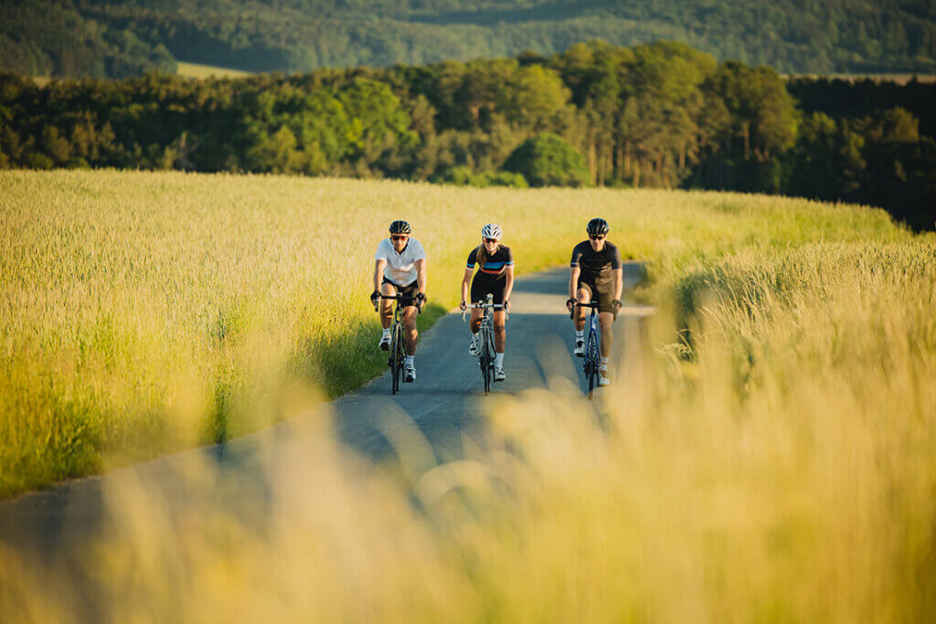 Drei Radfahrer genießen eine entspannte Radtour auf einem ländlichen Weg durch eine malerische Landschaft bei Sonnenschein.