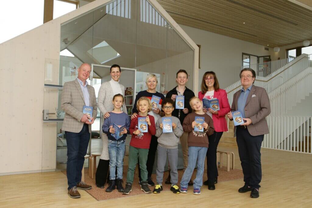 Aloha Buchübergabe VS Oberwart Eine Gruppe von Erwachsenen und Kindern hält Bücher in einer Bibliothek, die Bildung und Gemeinschaft bei Prima Magazin zeigt.