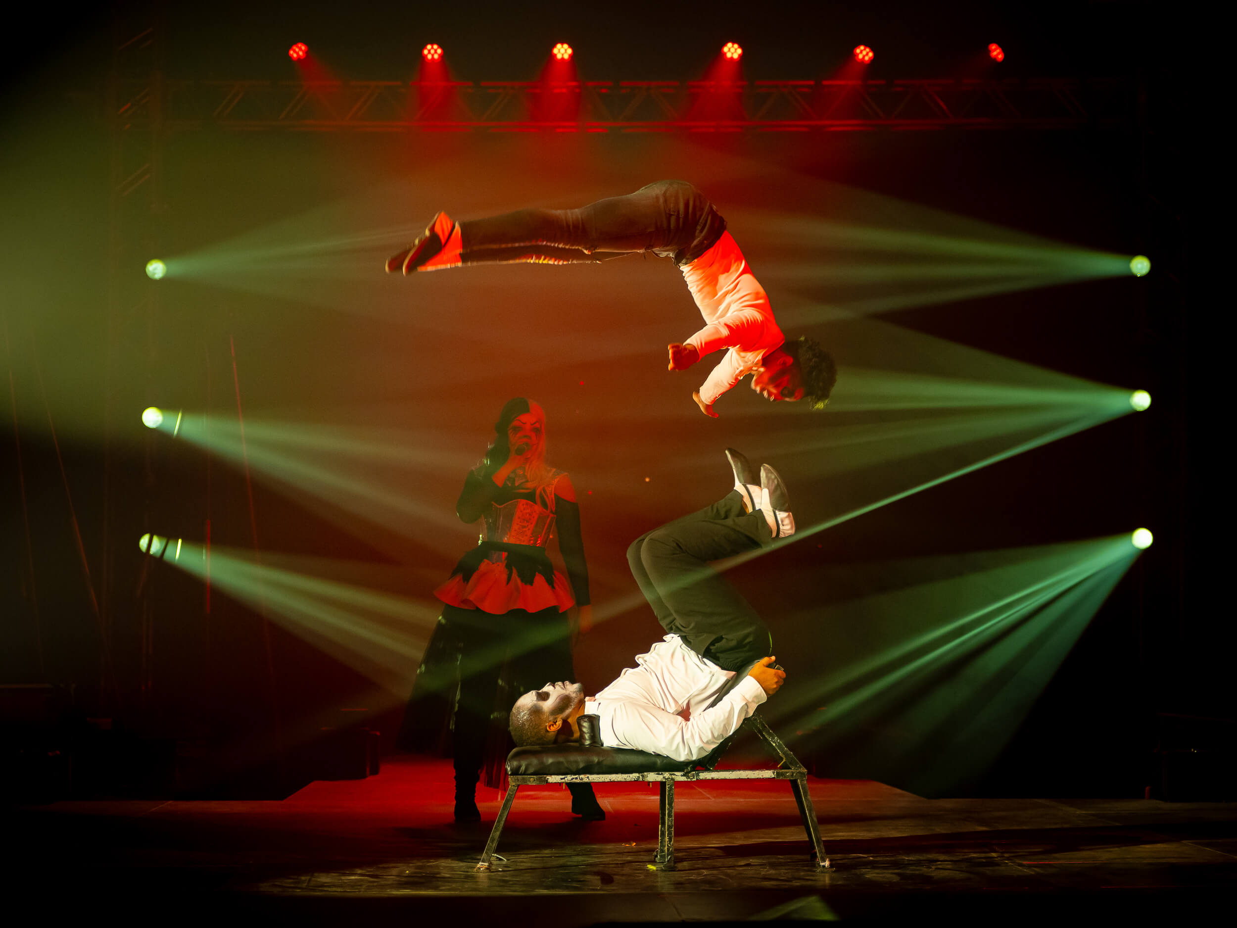 Akrobaten führen beeindruckende Tricks mit leuchtenden Lichteffekten auf der Bühne auf, während eine Frau zuschaut.