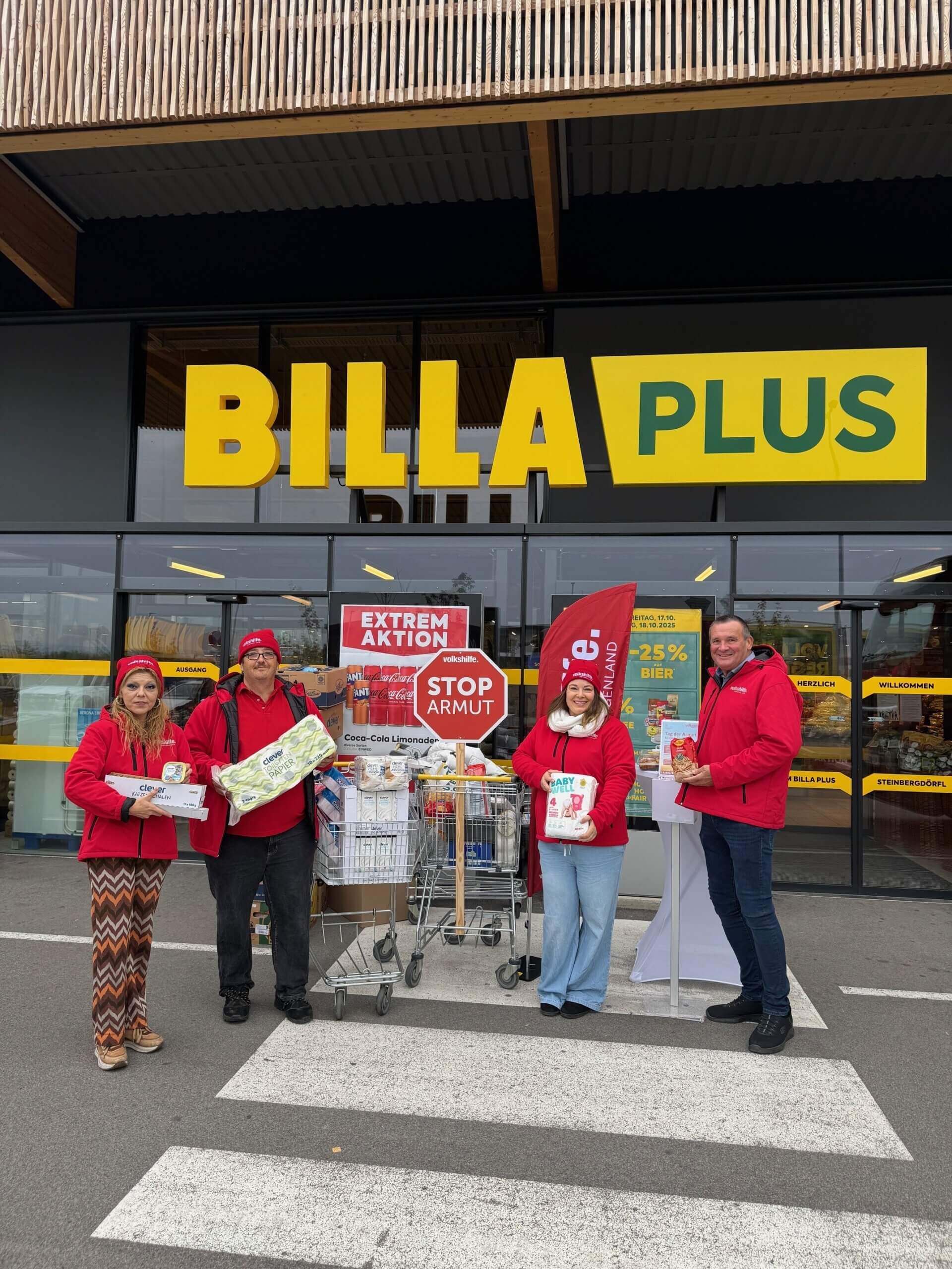 Menschen in roten Jacken sammeln Spenden gegen Armut vor einem BILLA PLUS Supermarkt, um Bedürftige zu unterstützen.