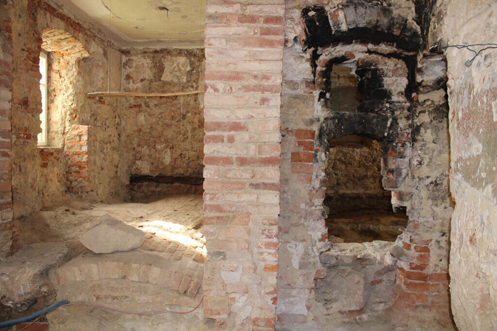 Ein altes Mauerwerk mit freigelegtem Backstein und Gewölbe in einem renovierungsbedürftigen Raum, beleuchtet vom Tageslicht.