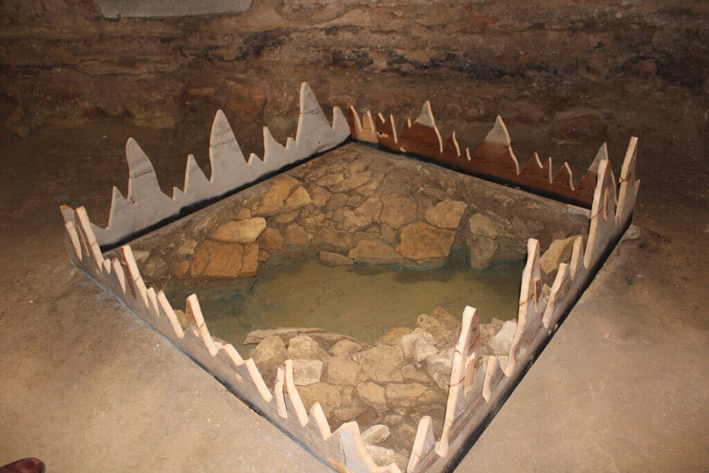 Steinmauer und Wasserstelle in rustikaler Umgebung, umgeben von dekorativen Zäunen; möglicherweise historischer Ort.