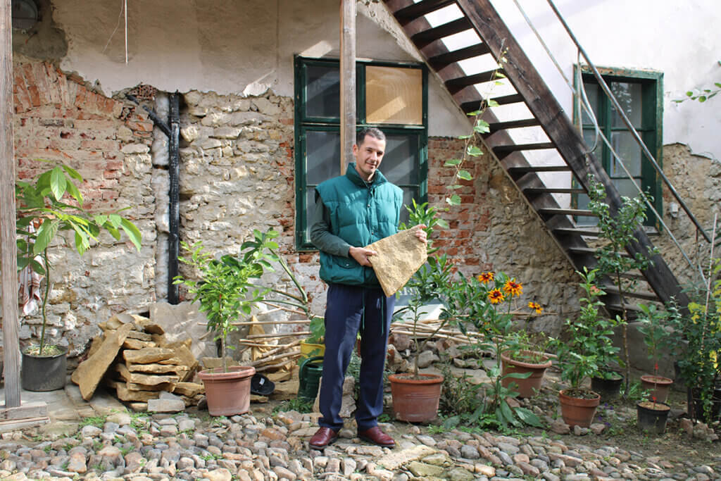 Haus lebt 9 © Nicole Matsch Person im Garten hält großen Stein vor historischem Gebäude mit Backsteinfassade und Pflanzen, für Prima Magazin fotografiert.