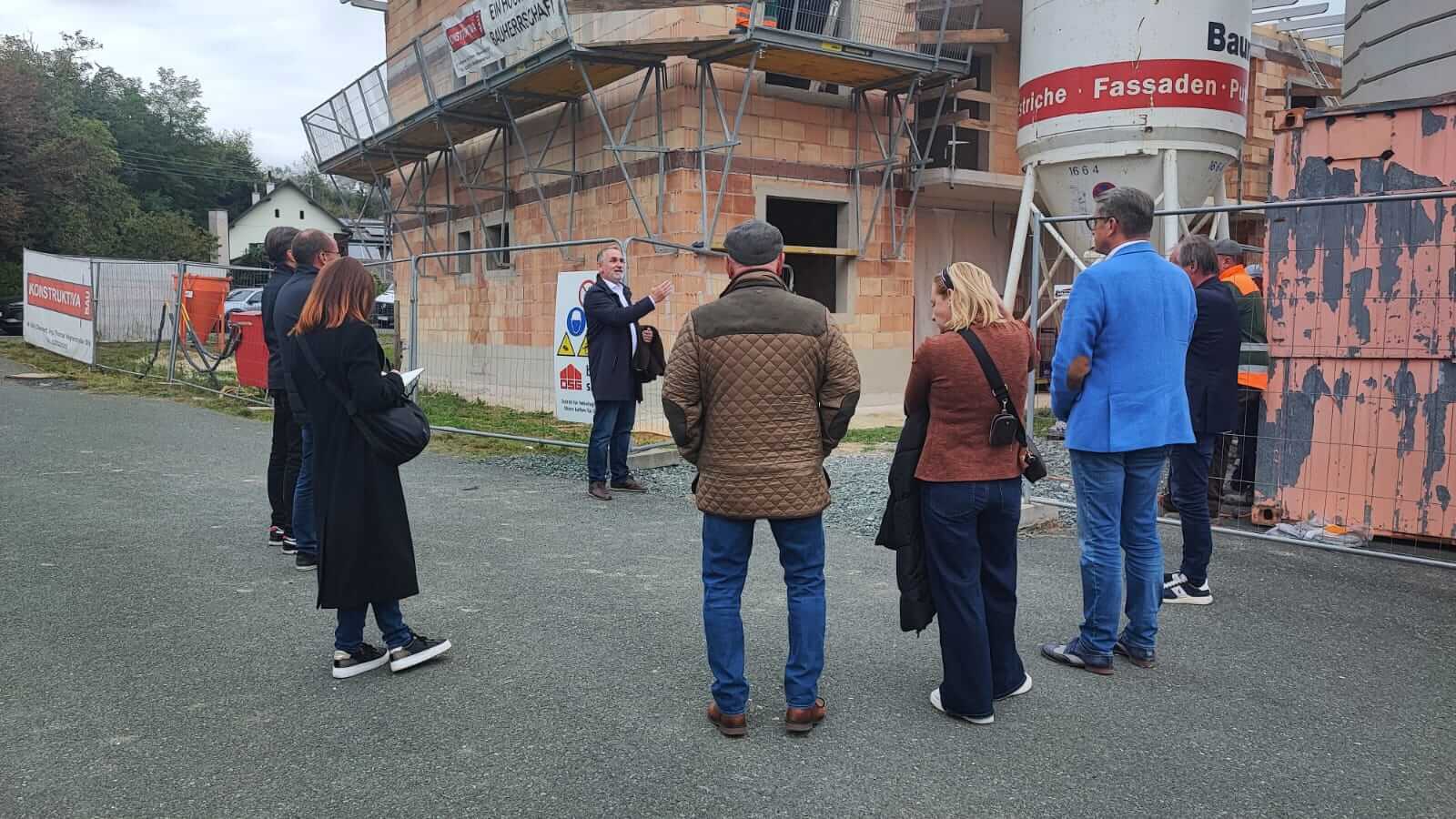 Personengruppe bei einer Besichtigung eines regionalen Bauprojekts, geführt von einem Experten, vor einem im Bau befindlichen Gebäude.