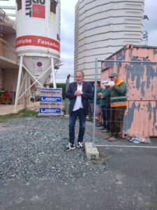 Eine Person spricht vor Baucontainern und Silos auf einer Baustelle. Kontext: Bauberichterstattung für Prima Magazin.