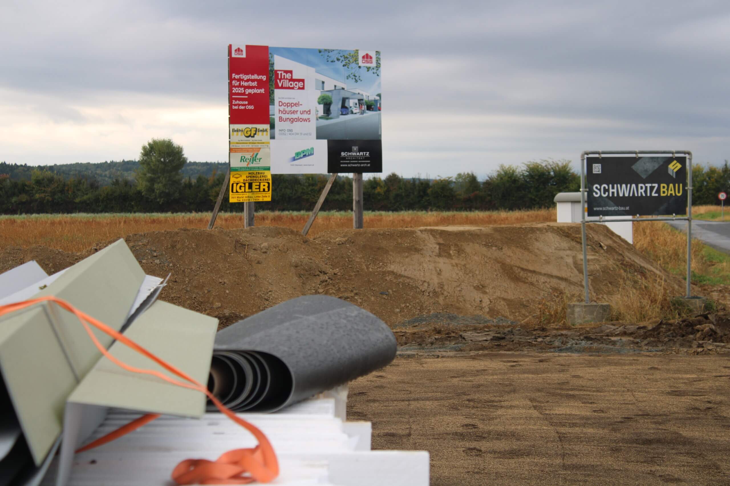 Baustellenschild kündigt neues Wohnprojekt „The Village“ mit Doppelhäusern und Bungalows an, Fertigstellung bis 2025.