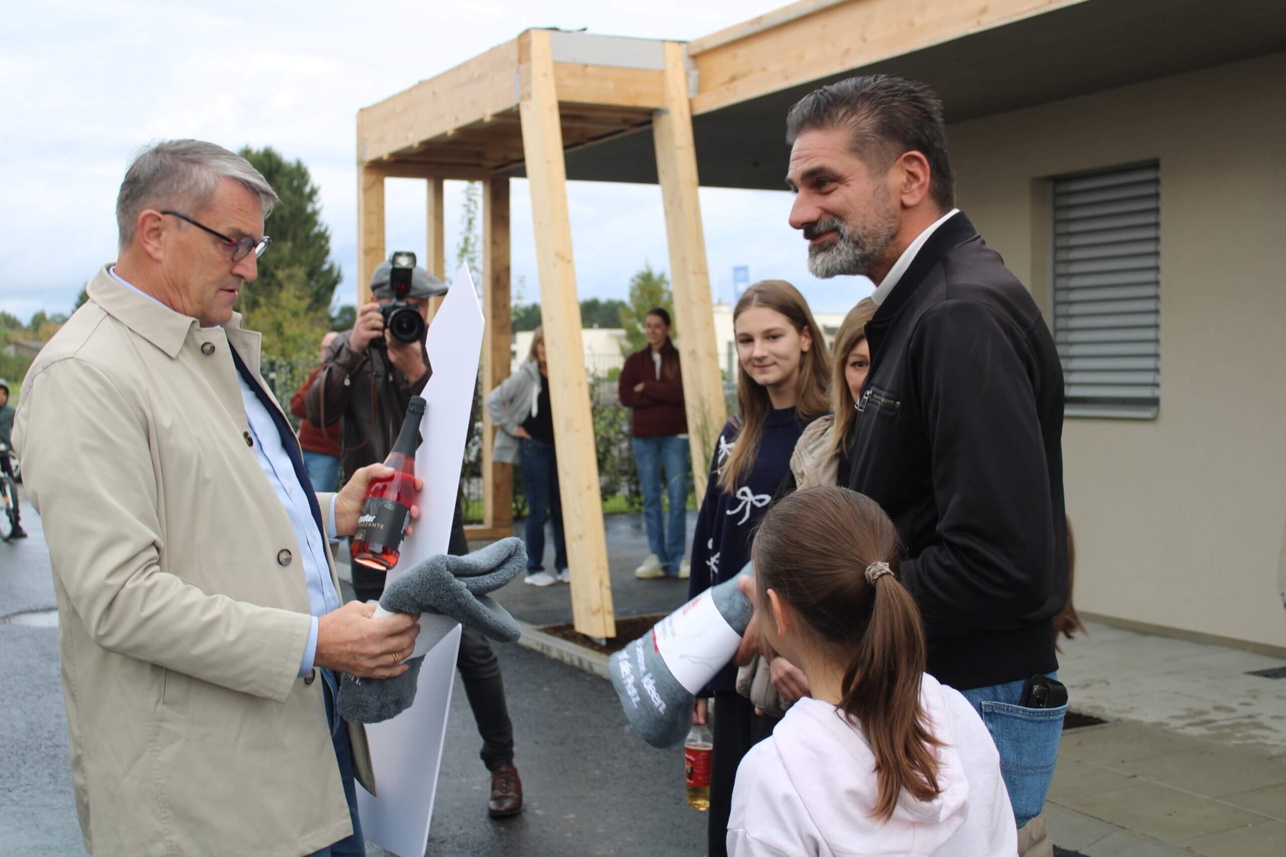 Menschen bei einer Feier im Freien, ein Mann übergibt einem anderen ein Geschenk, Kameramann hält den Moment fest.