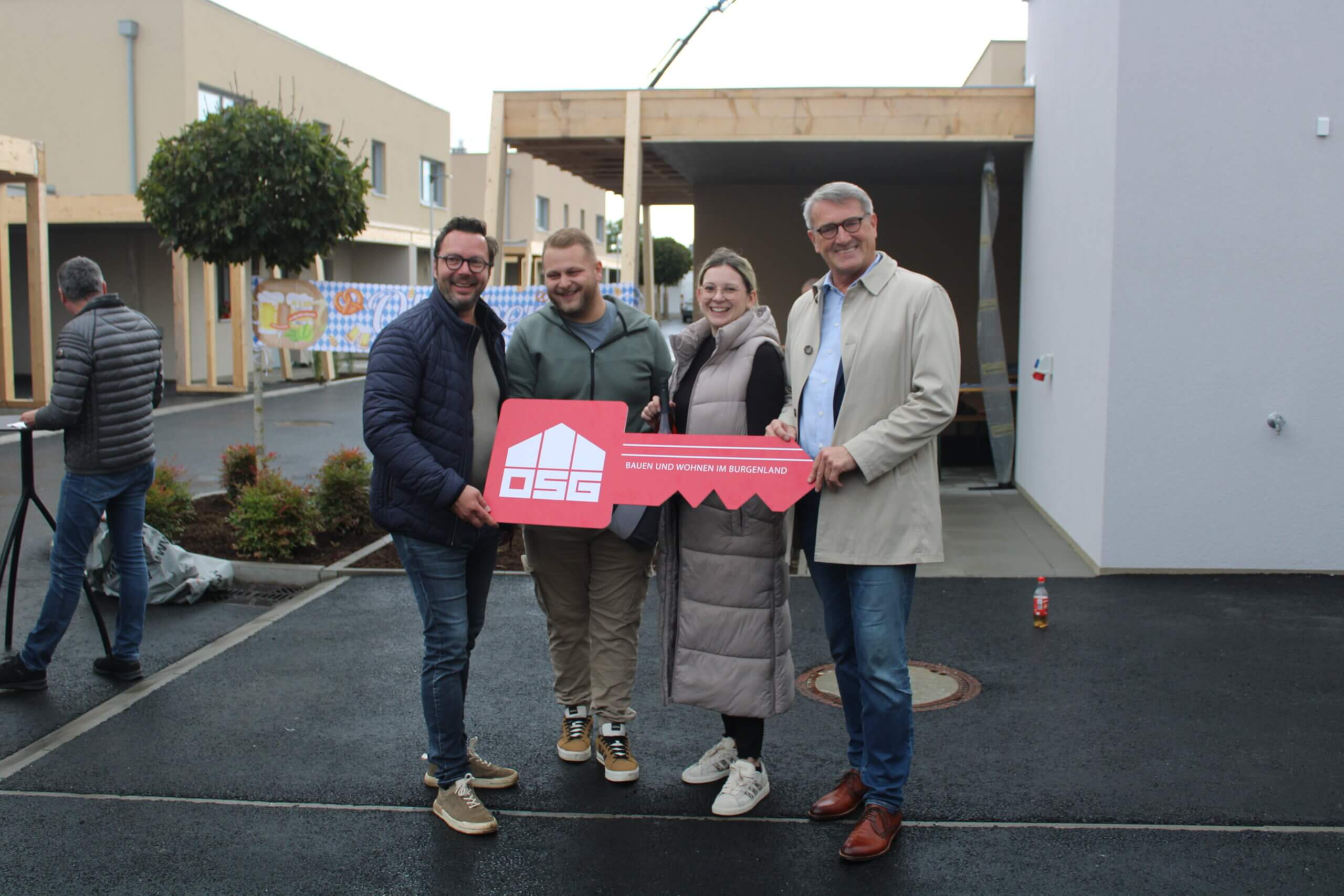 Vier Personen halten einen symbolischen roten Schlüssel vor einem neuen Wohnkomplex als Teil eines Projekts im Burgenland.