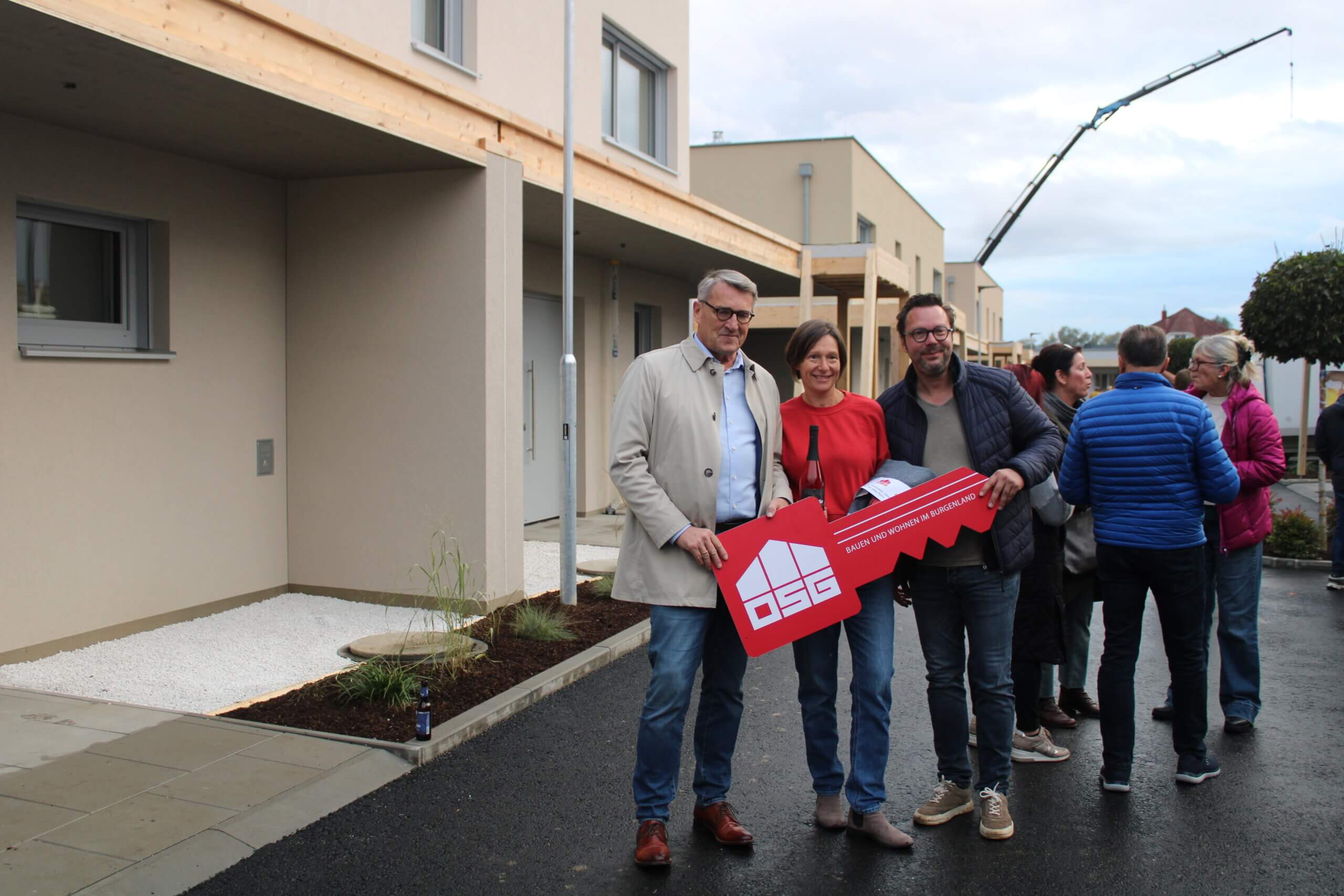 Gruppe beim Einweihungsfest für neues Wohnprojekt, hält symbolischen Schlüssel und feiert modernes Bauen im Burgenland.