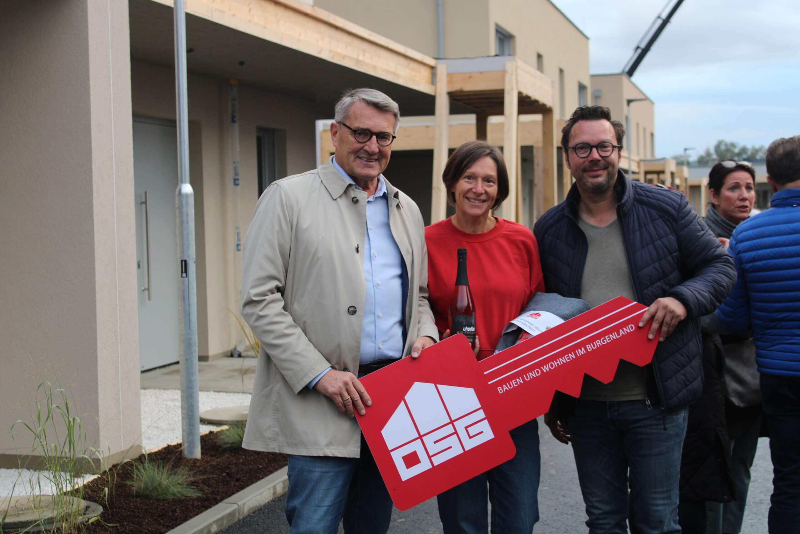 Drei Personen halten symbolischen Schlüssel vor Neubau, vermutlich Einweihungsfeier im Burgenland, fotografiert für Prima Magazin.