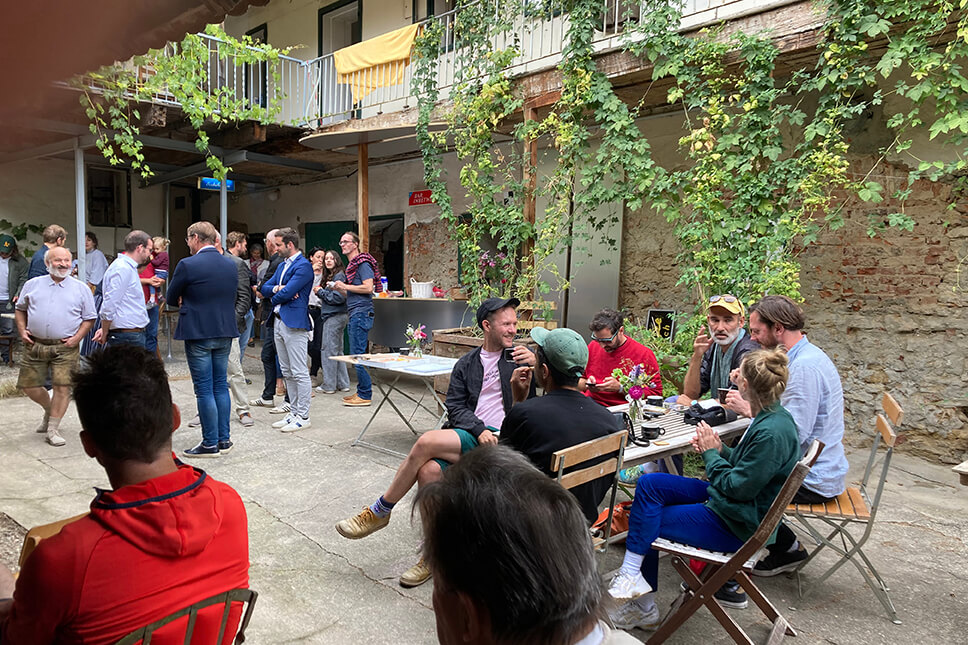 Innenhof (c) Hilde Swider Geselliges Treffen im begrünten Innenhof bei einem regionalen Event, Gäste unterhalten sich entspannt bei Getränken und kleinen Speisen.