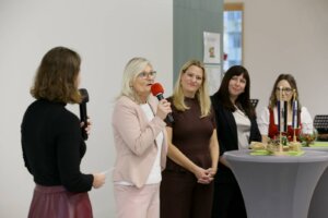 Eine Frau spricht am Mikrofon bei einem Netzwerktreffen, umgeben von Kolleginnen, vor einem Stehtisch im Kontext von Prima Magazin.