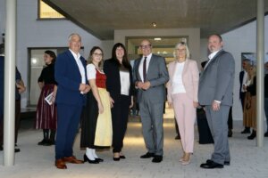 Eine Gruppe von Menschen in Geschäftskleidung und Tracht posiert bei einer Abendveranstaltung vor einem modernen Gebäude.