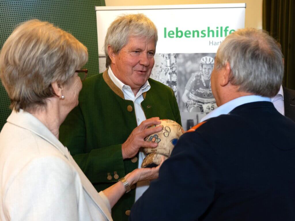 Mann in traditioneller Kleidung präsentiert einem kleinen Publikum einen bemalten Ball bei einer Veranstaltung der Lebenshilfe Hartberg.