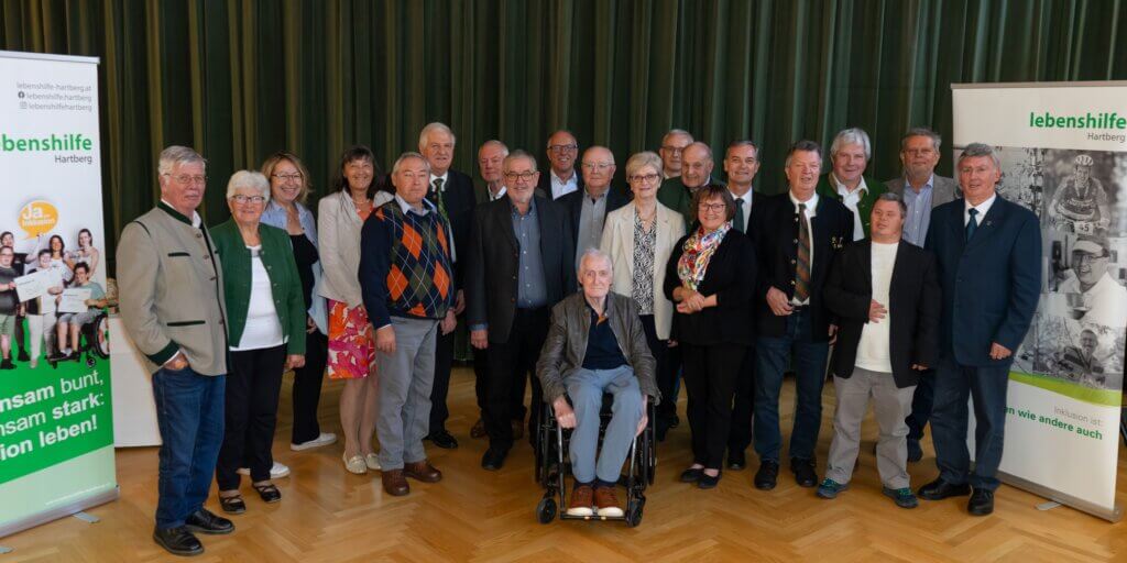 Eine Gruppe von Menschen bei einem Event der Lebenshilfe Hartberg, lächelnd vor grünen Bannern.