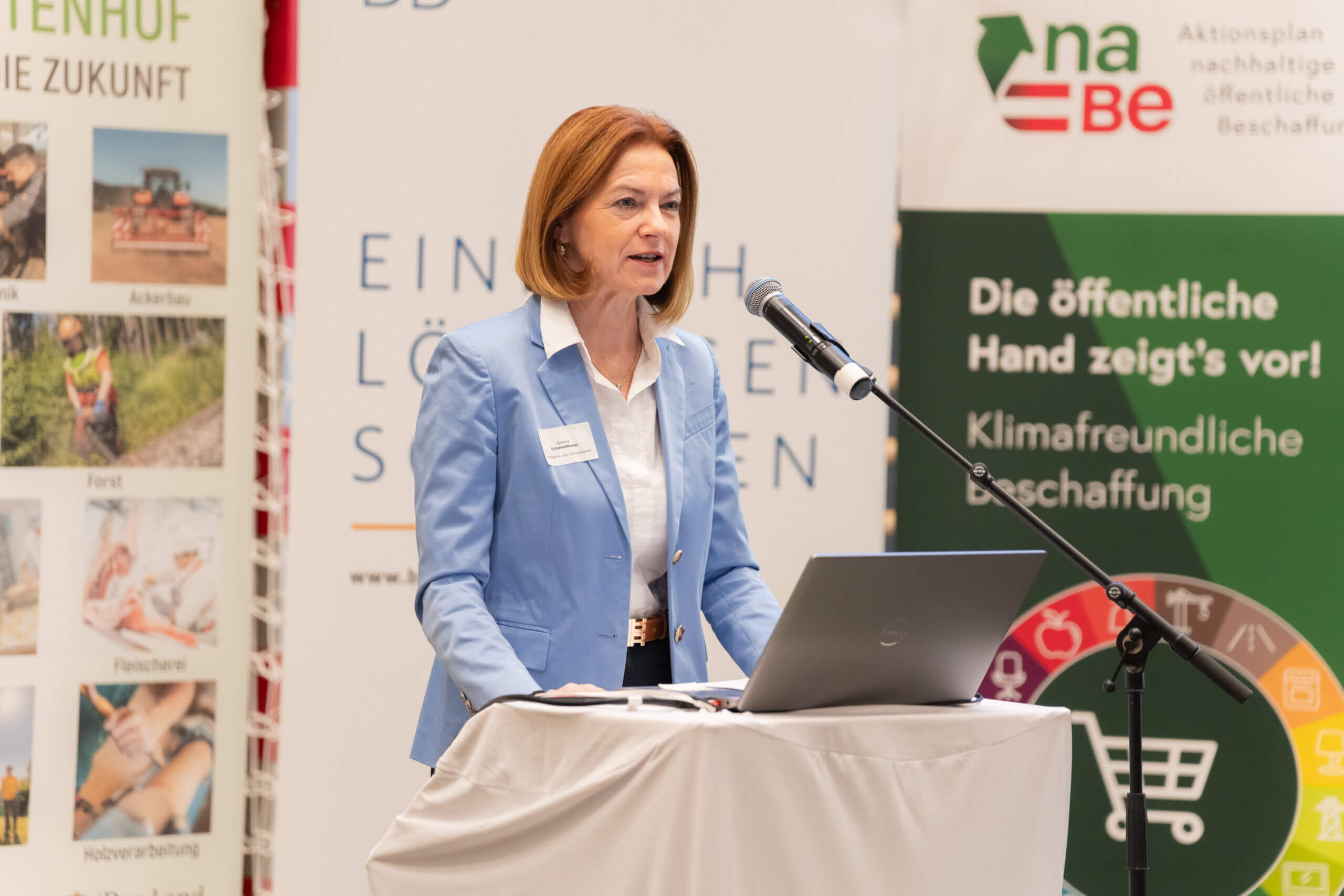 Rednerin bei einer Konferenz zum Thema nachhaltige Beschaffung, präsentiert vor Bannern mit Umweltbotschaften.