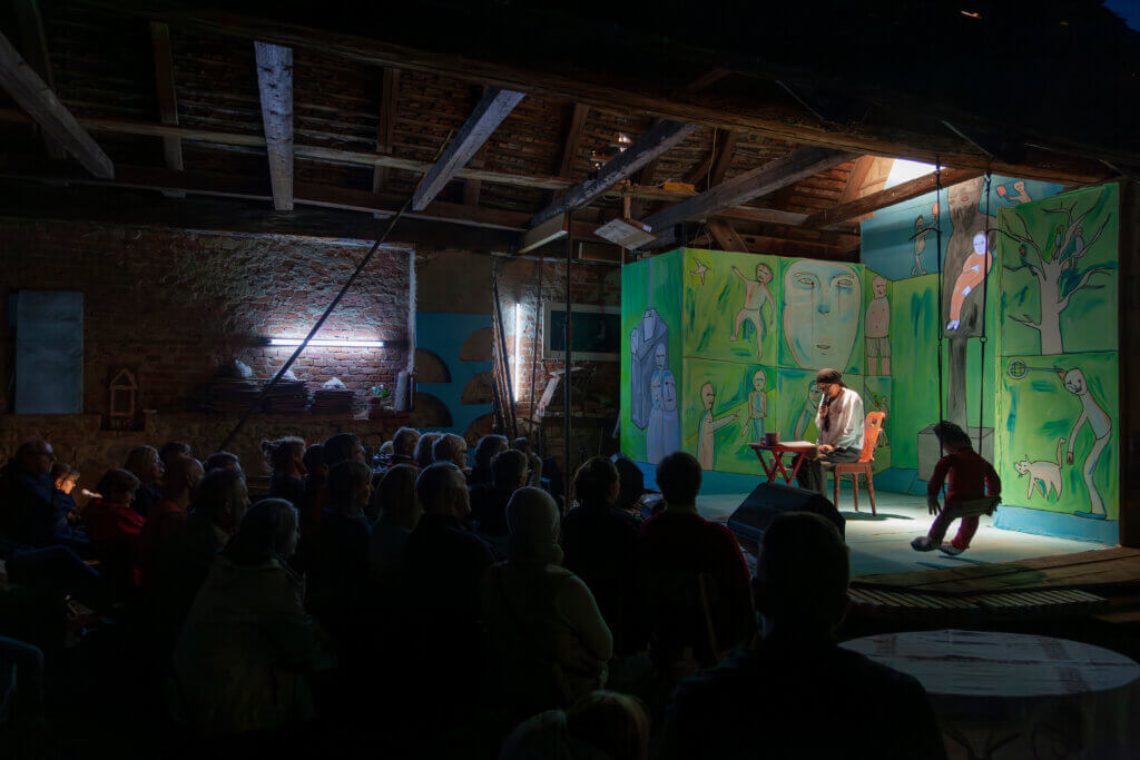 Ein Theaterstück in einem rustikalen Raum fesselt Zuschauer mit bunter Kulisse und intensiver Darbietung.