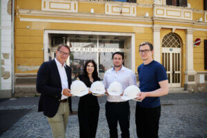 Personen vor einer Bäckerei, die Bauhelme halten, symbolisieren den Beginn eines regionalen Bauprojekts beim Prima Magazin.