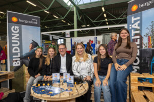 Gruppenfoto bei einer Bildungsmesse im Burgenland, mit jungen Erwachsenen und Veranstaltern an einem Info-Stand für Bildung.