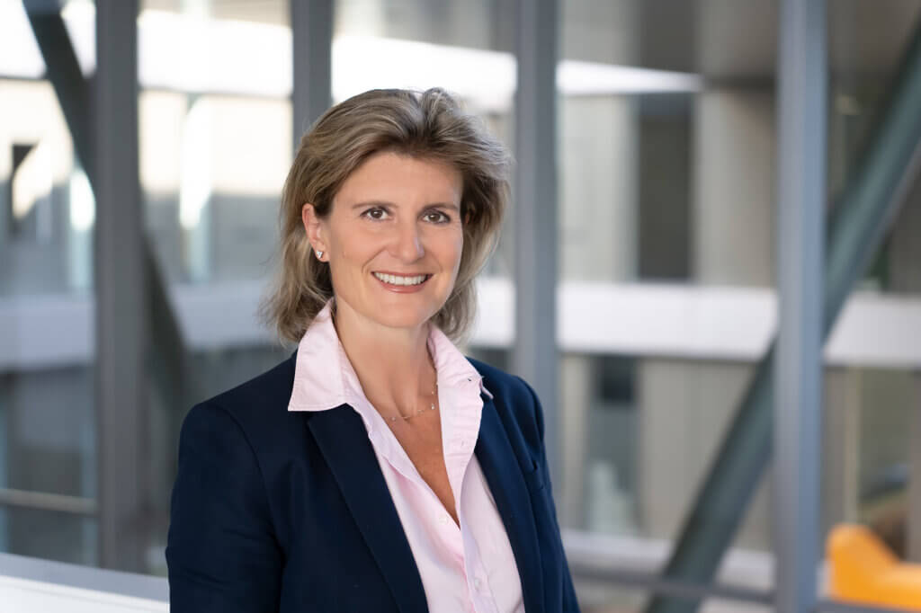 Schauer-Frank_Bettina_Pressebild©HochschuleBurgenland Lächelnde Frau in Business-Kleidung vor modernen Bürofenstern, symbolisiert Expertise im regionalen Qualitätsjournalismus.