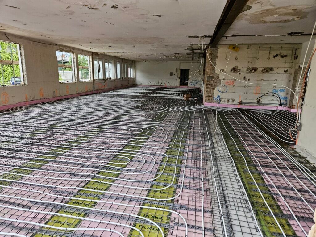 Unknown©PIK SÜD Gmbh Renovierungsprojekt: Ein leerer Raum mit verlegten Heizungsrohren auf dem Boden, bereit für weitere Bauarbeiten.