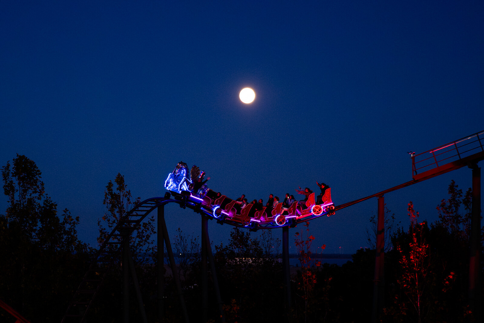 Beleuchtete Achterbahn vor Vollmond am Nachthimmel, symbolisch für spannende regionale Erlebnisse.
