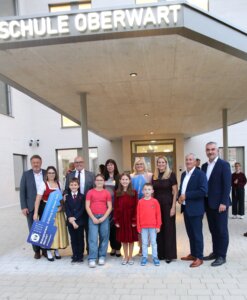 Gruppe aus Erwachsenen und Kindern bei der Eröffnung der Schule Oberwart, festlich gekleidet vor dem Eingang versammelt.
