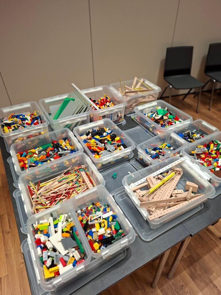 Kisten mit bunten Bausteinen und Holzstäben auf einem Tisch, bereit für kreatives Bauen, im Kontext von Prima Magazin.