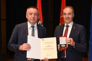 Zwei Männer bei einer Auszeichnung im Burgenland, einer hält eine Urkunde, der andere eine Medaille. Offizieller Anlass.