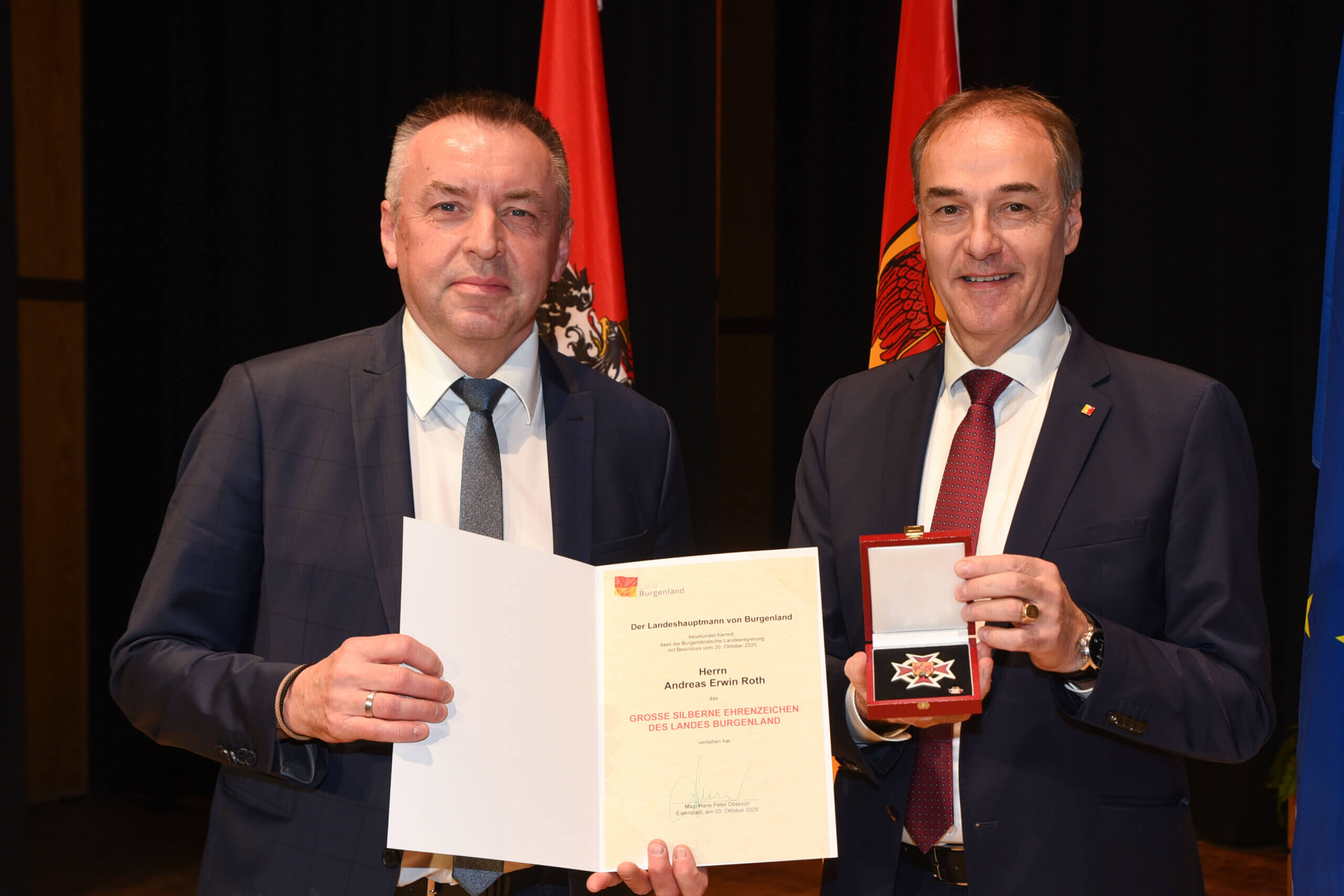 Zwei Männer bei einer Auszeichnung im Burgenland, einer hält eine Urkunde, der andere eine Medaille. Offizieller Anlass.