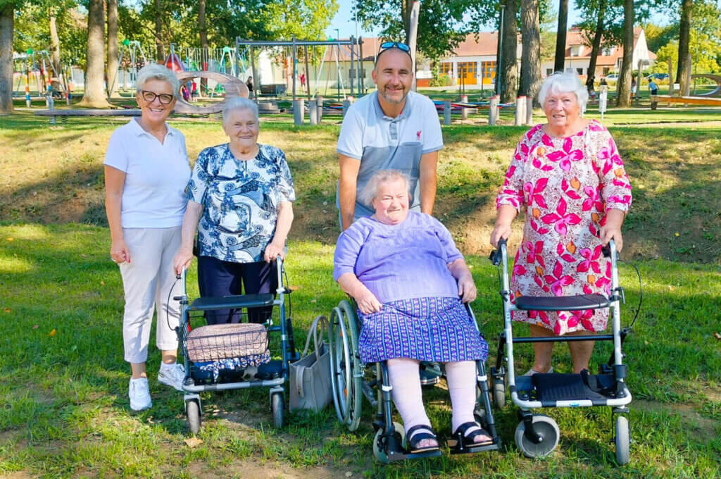 Gruppe von Senioren und Betreuern genießt sonnigen Tag im Park, Symbol für Gemeinschaft und Lebensfreude im Prima Magazin.